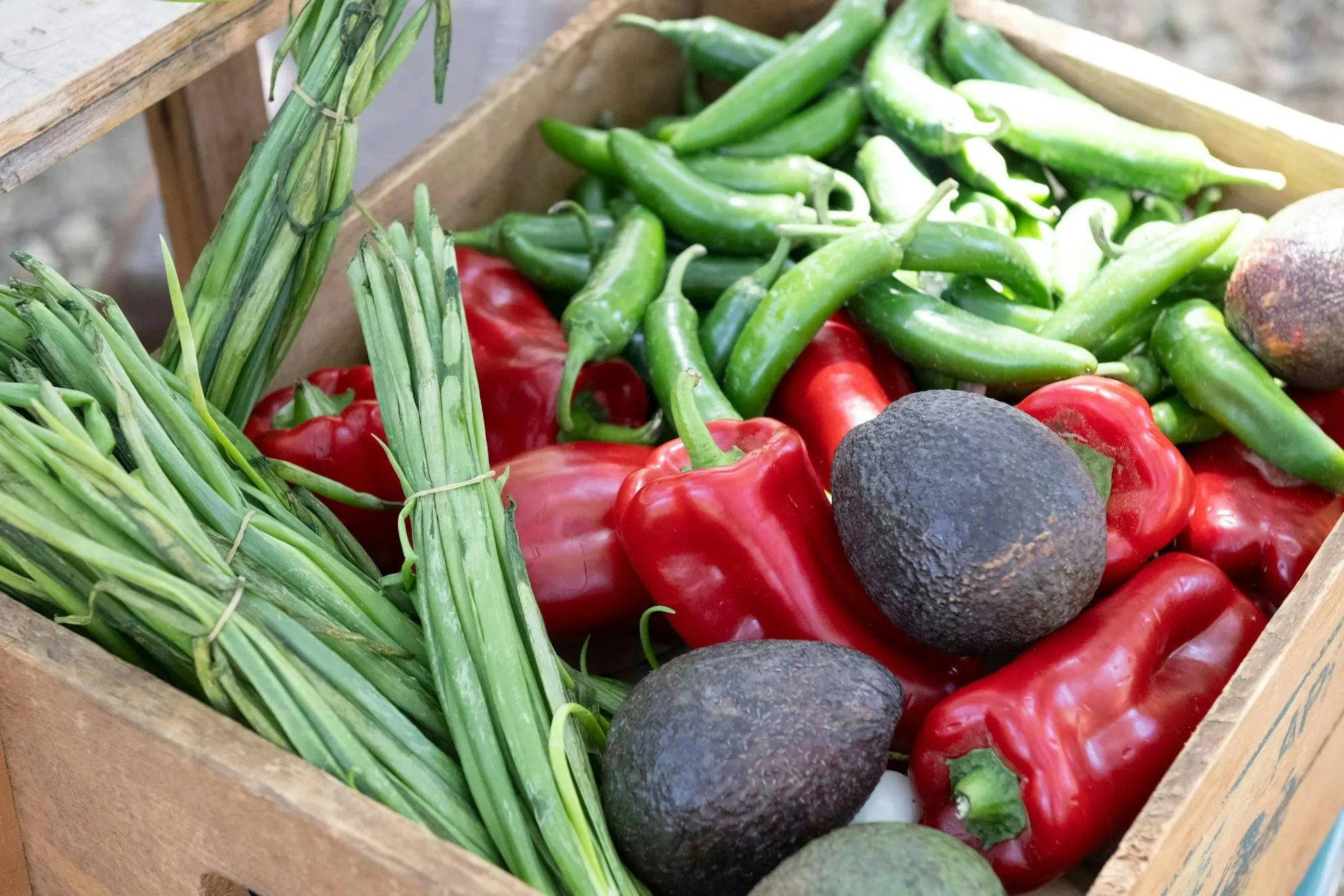 Close-up of red peppers, green chillies, runner beans and avocados in a wooden crate